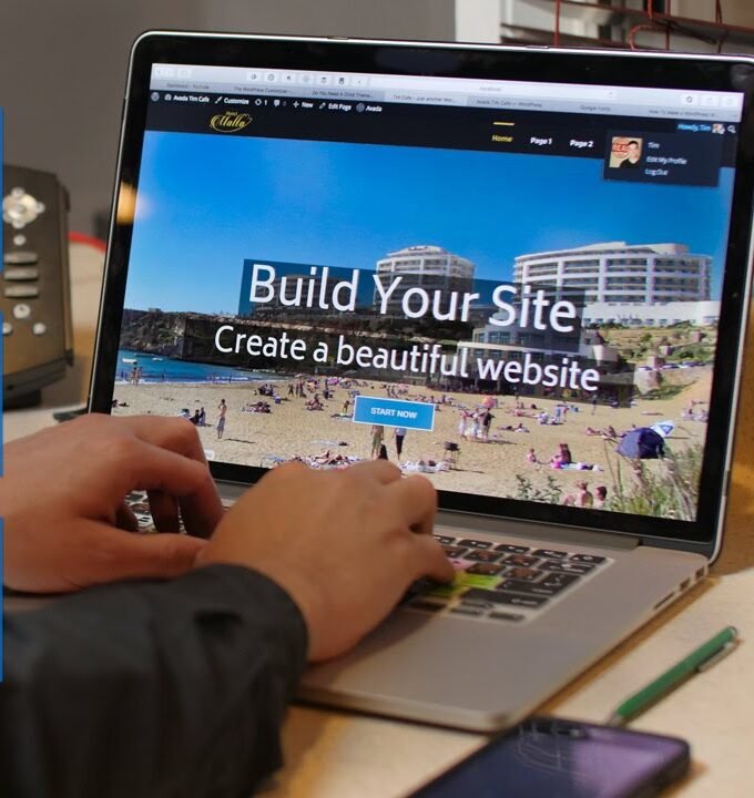 Person using a laptop to build a website, with the screen showing a scenic beach homepage and overlaid text "Build Your Site - Create a beautiful website.